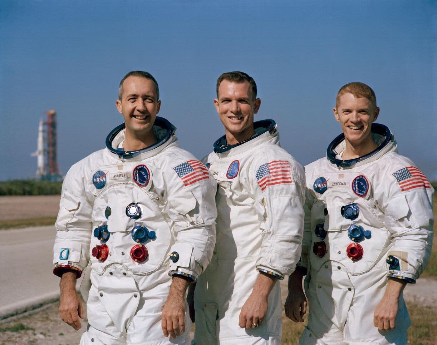 Posádka Apolla 9 (McDivitt, Scott, Schweickart) před startovní rampou se Saturnem V v pozadí (NASA).