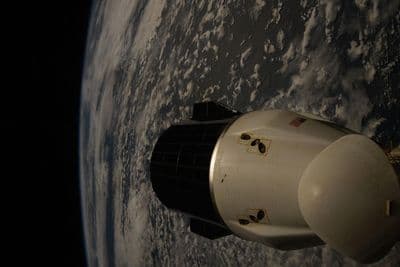 Kosmická loď Dragon od SpaceX na oběžné dráze nad zataženou Zemí, zadokovaná u Mezinárodní vesmírné stanice.