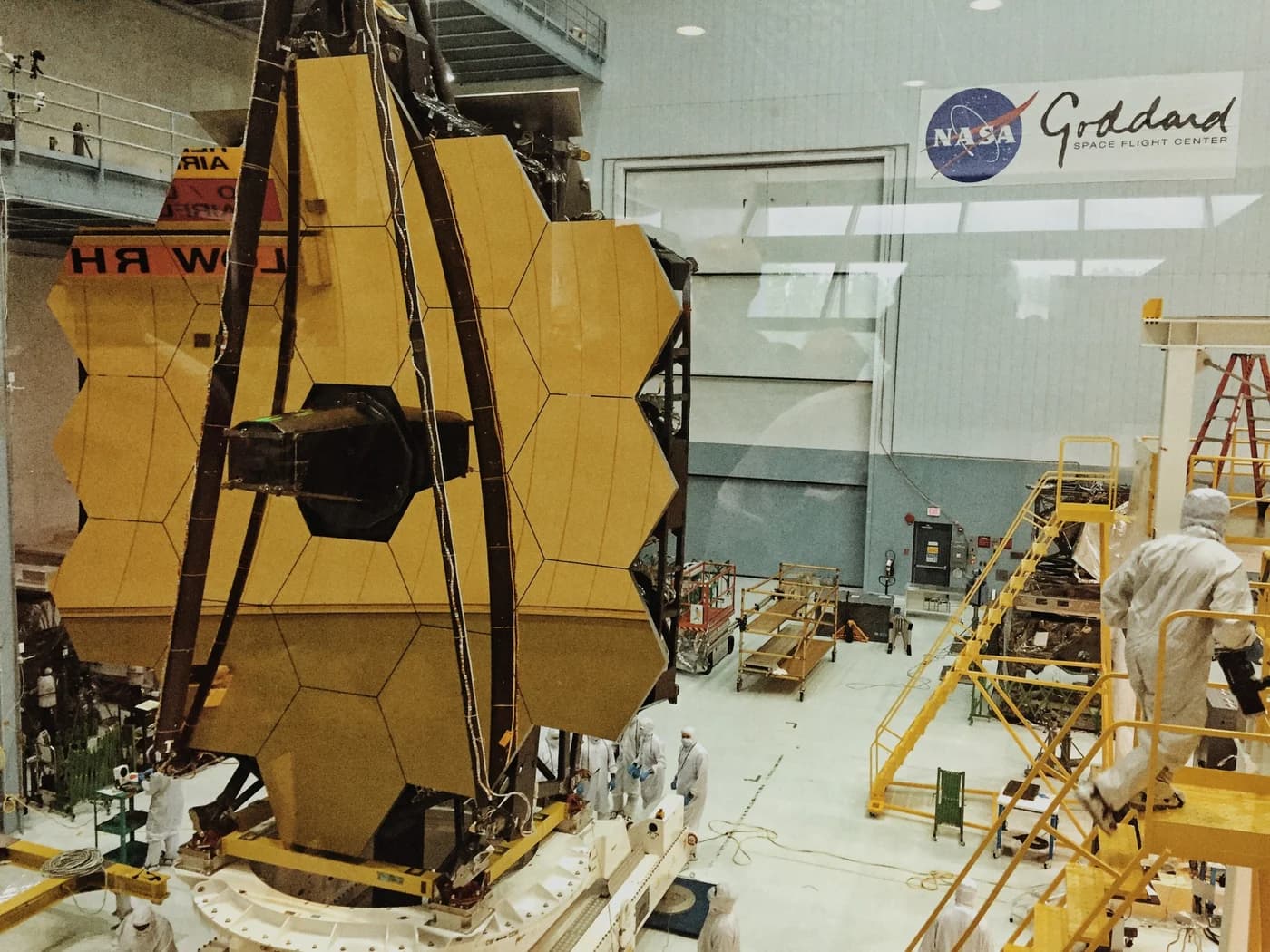 The assembled telescope, with its 18 gold-coated primary mirror segments and the secondary mirror on its support struts, seen face-on through the observation window of the cleanroom at NASA's Goddard Space Flight Center.