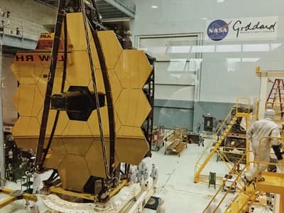 The assembled telescope, with its 18 gold-coated primary mirror segments and the secondary mirror on its support struts, seen face-on through the observation window of the cleanroom at NASA's Goddard Space Flight Center.