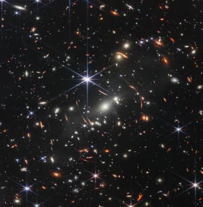 Webb's First Deep Field: a near-infrared NIRCam image of the galaxy cluster SMACS 0723, whose gravity bends and magnifies the light of more distant galaxies behind it. Released in July 2022.