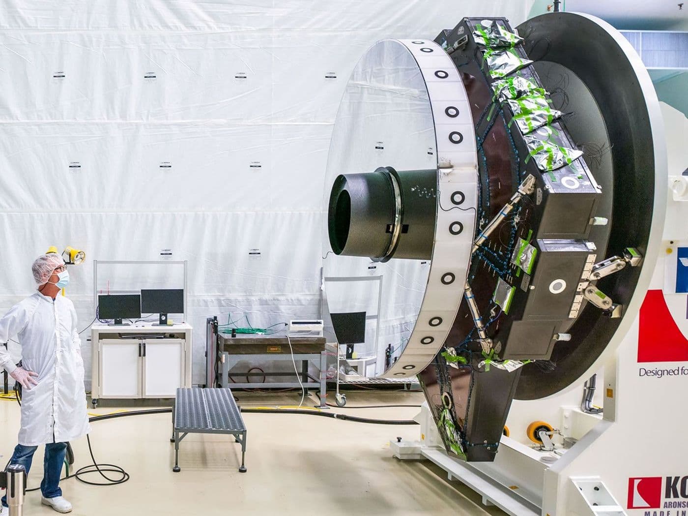 A NASA optical engineer inspects the surface of the Nancy Grace Roman telescope's primary mirror in a clean room.