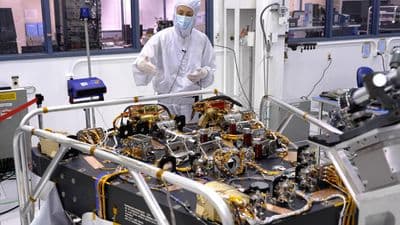 Technik v ochranném oděvu pracuje vedle optické sestavy koronografu Romanova teleskopu v čisté hale JPL.