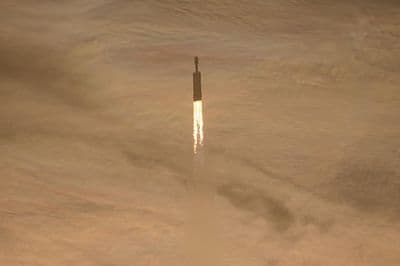 The Falcon Heavy rocket with the Nancy Grace Roman telescope climbs after launch above the Kennedy Space Center through clouds tinted by morning light.
