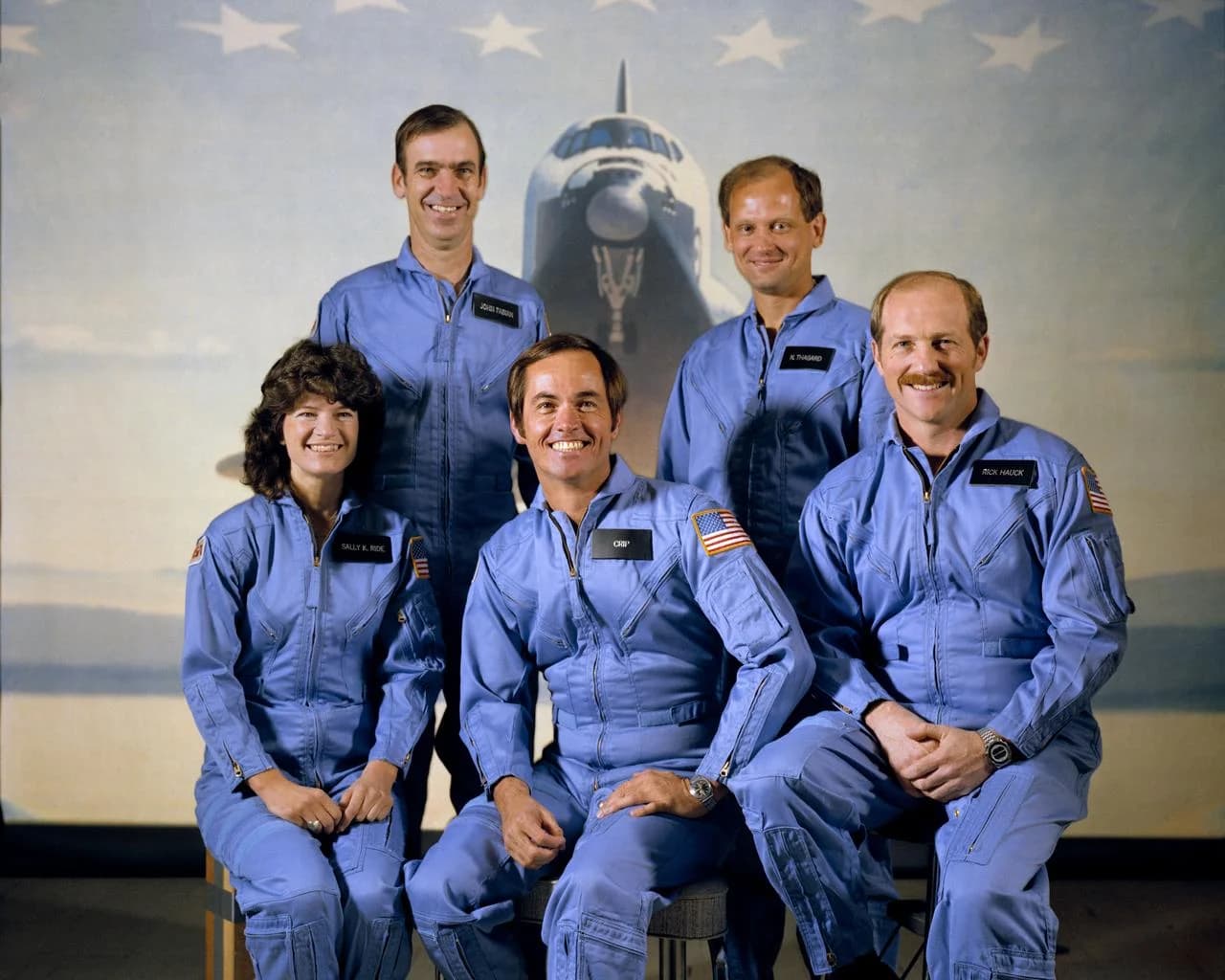 The STS-7 crew in March 1983. Sally Ride is seated at left, commander Robert Crippen at center and pilot Frederick Hauck at right; John Fabian and Norman Thagard stand behind them. NASA, S83-29016.