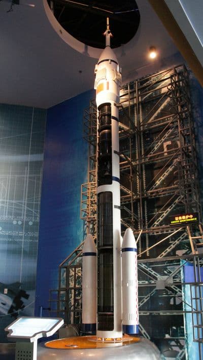 Plnorozměrný model pilotované rakety Dlouhý pochod 2F se záchrannou věží na špičce a čtyřmi pomocnými motory po stranách, vystavený v muzeu.