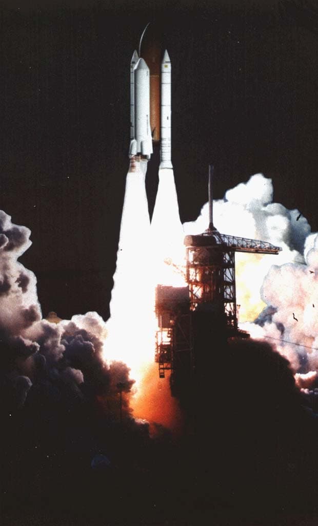 Koncepční malba nákladního nosiče Shuttle-C stoupajícího po startu nad oblakem kouře.